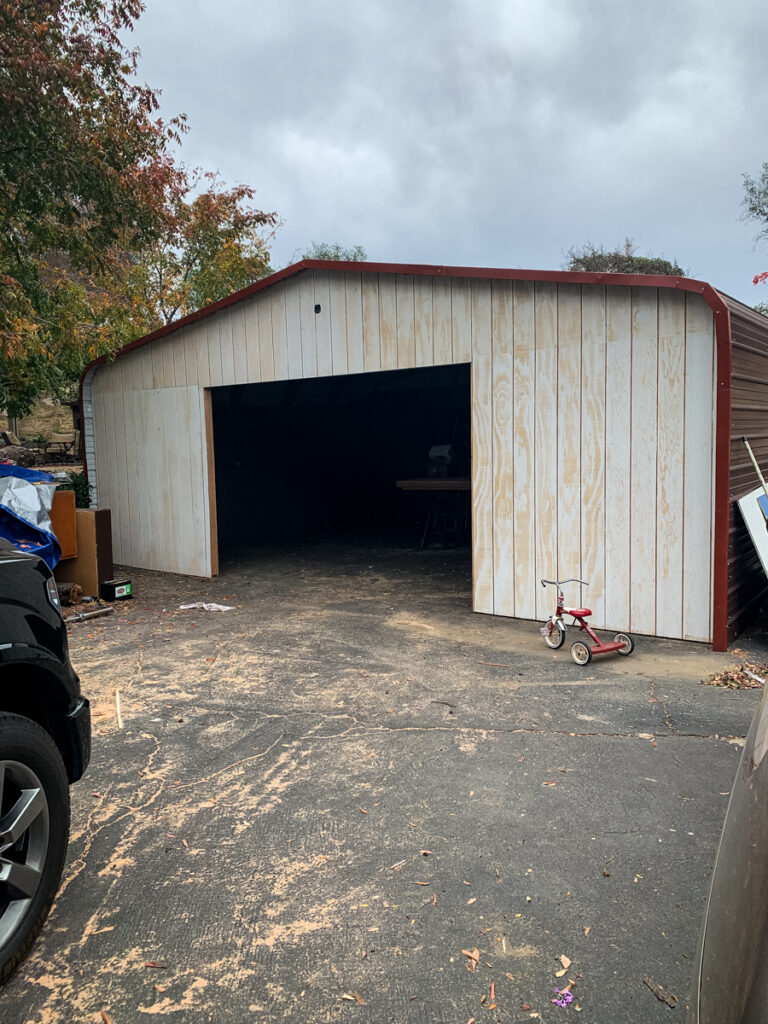 Photo of the front siding being added to the carport and a coat of primer being applied.