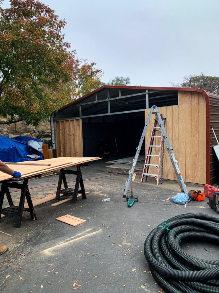 The photo shows metal siding and wooden studs to frame out the front of the carport barn.