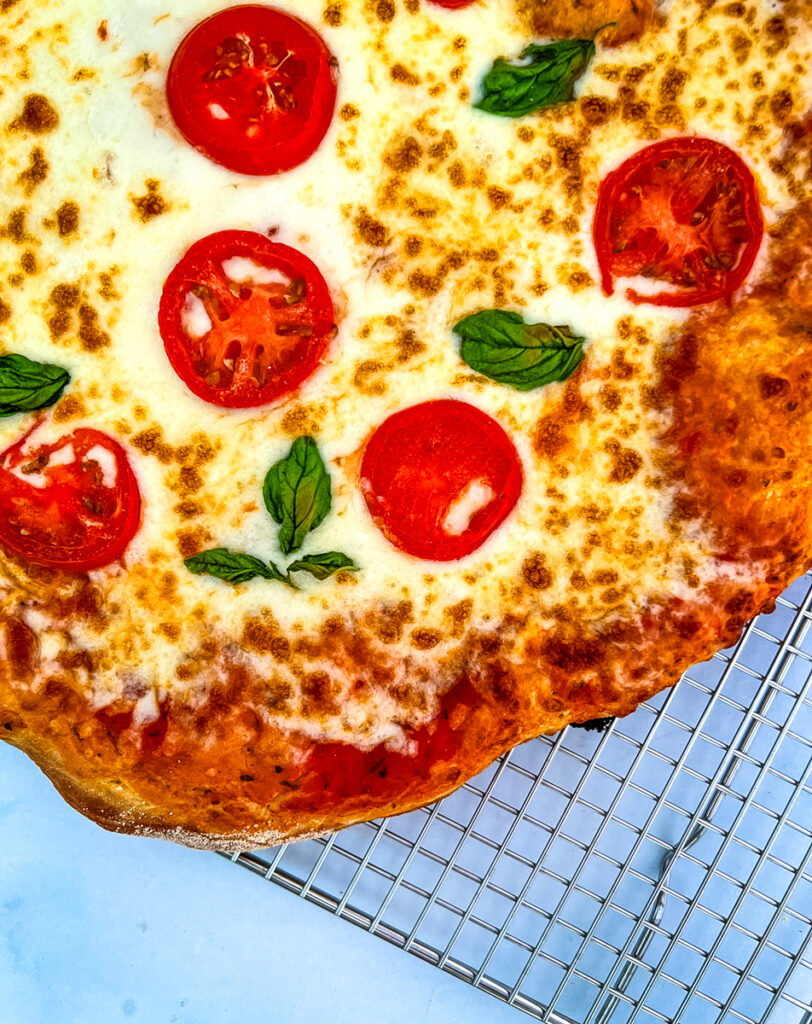 The photo shows a close up of a pizza with cheese, tomatoes and basil.