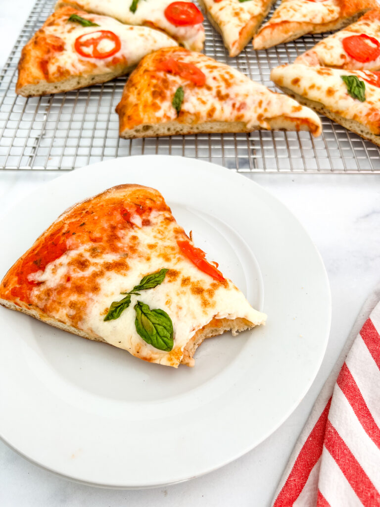 The photo shows sliced pieces of pizza on a cooling rack at the top with the focus on a piece of pizza with a bite taken out of it.
